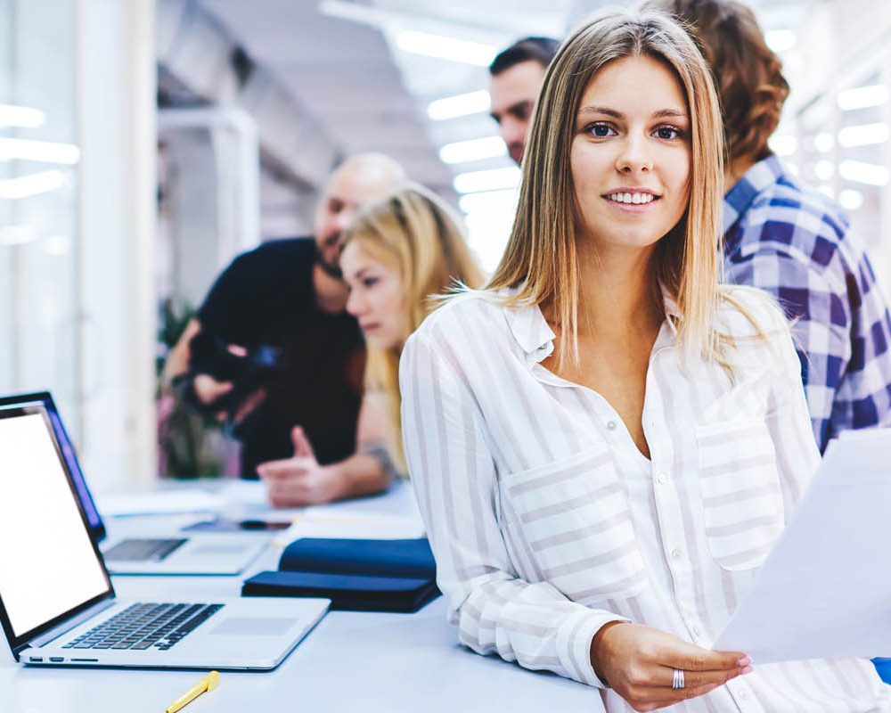 Portrait of young female team leader of talented journalists organizing work of members motivates and inspire them to make researching, standing on blurred background in modern coworking space